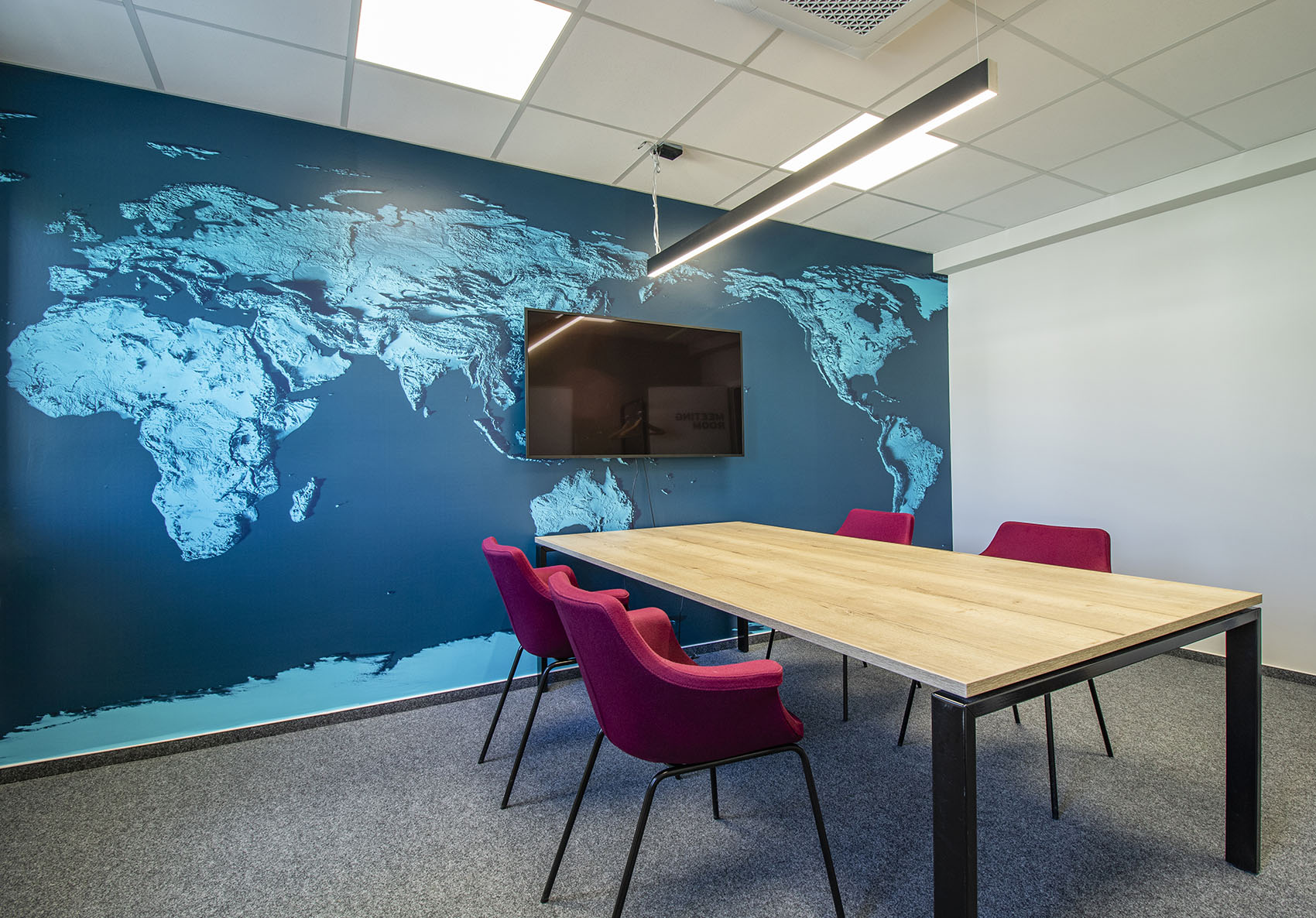 Wandgestaltung im Konferenzraum mit einer türkisblau eingefärbten Satellitenaufnahme der Erde. Beeren-farbige Konferenzstühle bietet einen perfekten Kontrast.