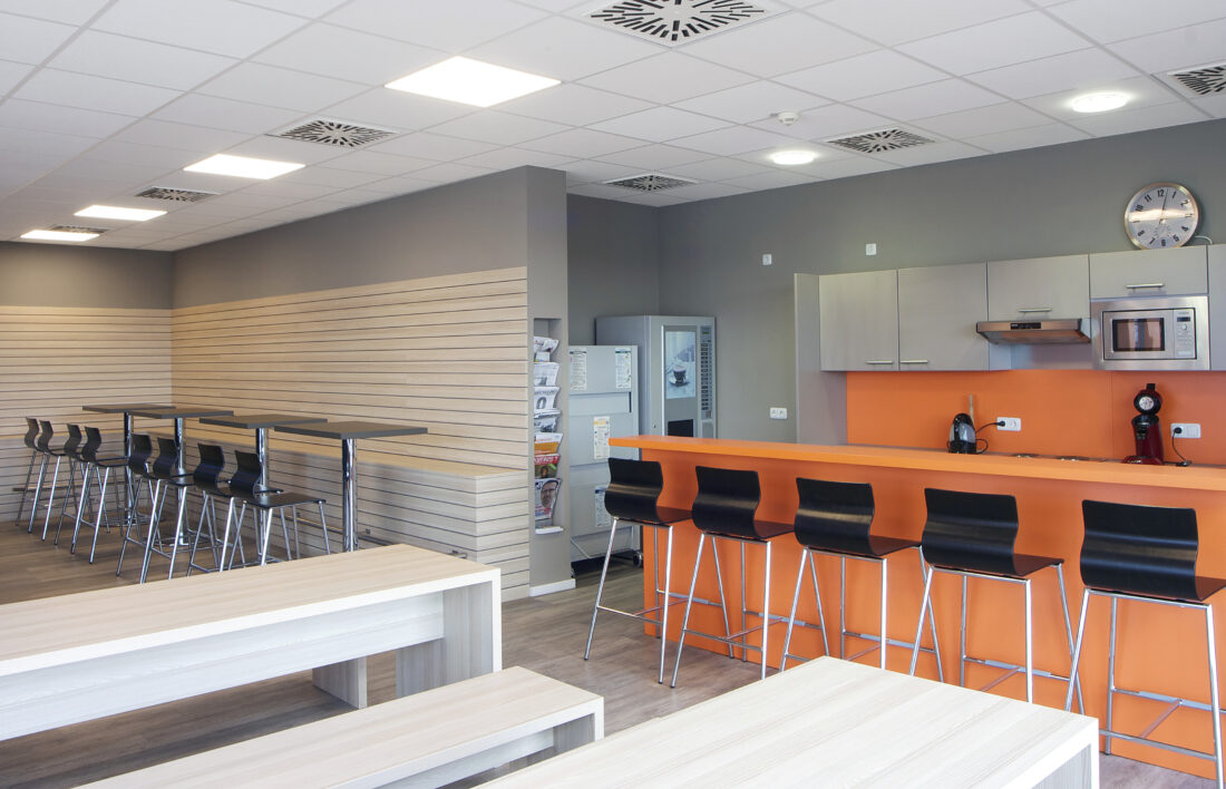 Küche mit orangen Bartresen und Barhockern. Sitzgelegenheit in Lamellenoptik und Stehtisch