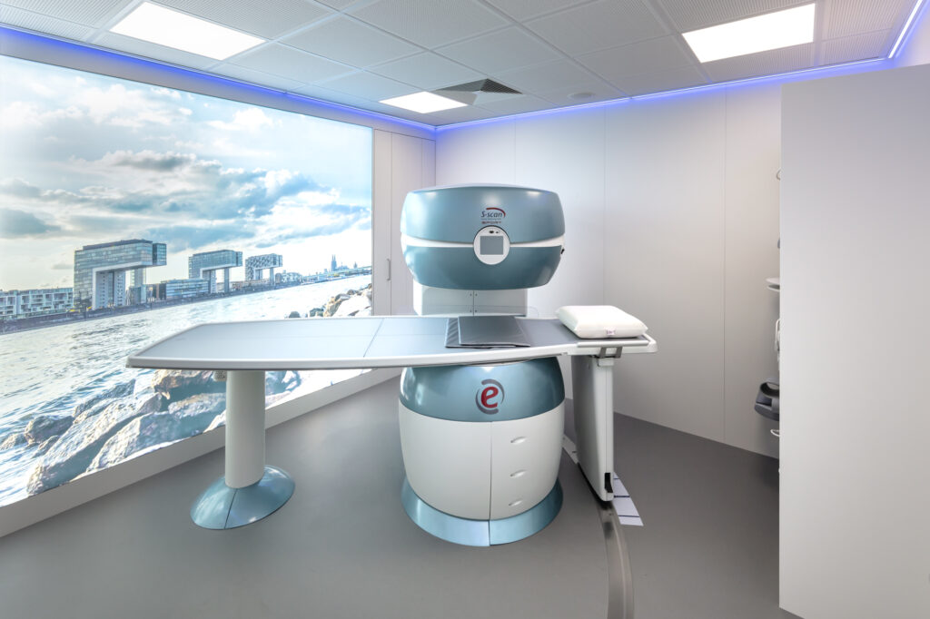 Das futuristische MRT mit großem Leuchtbild im Hintergrund und blauer, indirekter Beleuchtung an der Decke.