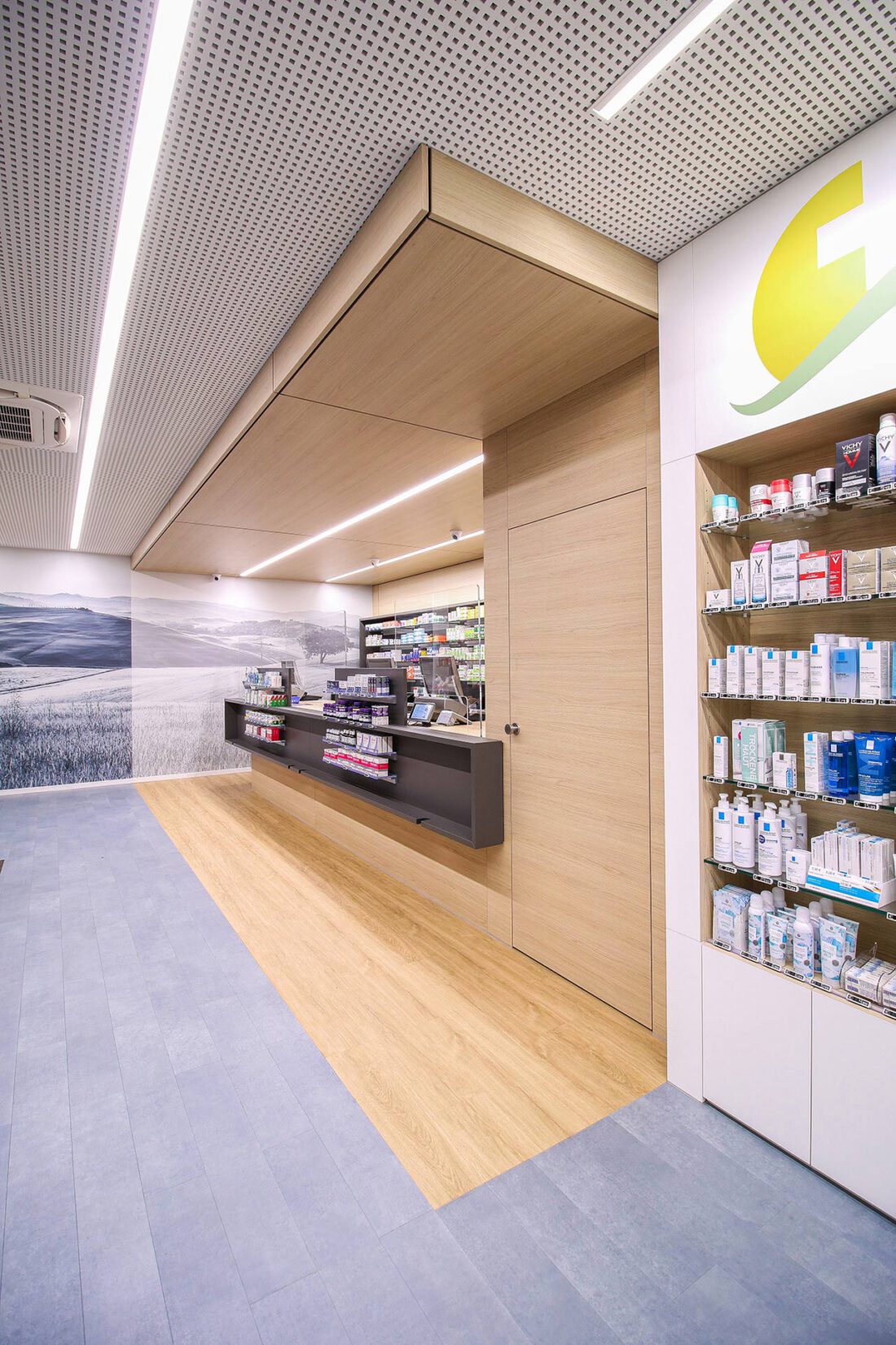 Moderne Apothekengestaltung mit Verkaufstresen, Holzoptik, integrierten Regalsystemen und Wandgestaltung mit Naturmotiv.